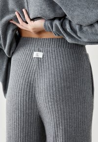 Person wearing high-waisted, ribbed grey knit pants with a "Cool Cosy Comfy" label and lifting a matching grey sweater.