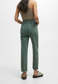 Jean vert taille haute, coupe décontractée avec ourlets retroussés. Dispose de deux poches arrière et d'une finition en tissu doux. Accompagné de mocassins beige.