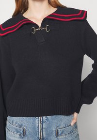 Mörkblå tröja med en bred sjömanskrage som har röda ränder och detaljer i guld. Ribbad nederkant och ärmar ger textur.