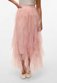 Ampia gonna maxi in tulle rosa pallido con volantes sovrapposti, vita elasticizzata e texture trasparente, abbinata a ballerine chiare.