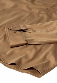 Braunes Langarmhemd mit geknöpften Manschetten und sichtbaren Nähten, flach ausgelegt mit einem über die Vorderseite gefalteten Ärmel.