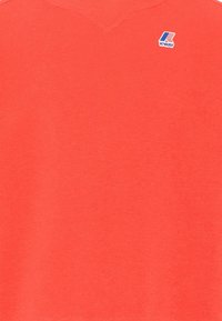 Tela naranja brillante con pequeño logo de K-Way en azul, blanco y rojo en la parte superior derecha.