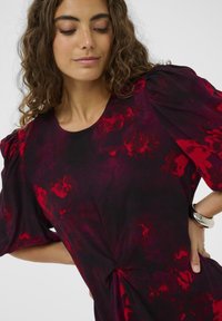 Rochie neagră cu modele florale abstracte în nuanțe de roșu, mâneci bufante și un detaliu legat la talie. Țesătură netedă cu un finisaj ușor texturat.