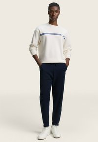 Sudadera de marfil con rayas marinas en el pecho, combinada con pantalones jogger marinos y zapatillas blancas, con un ajuste relajado y puños acanalados.