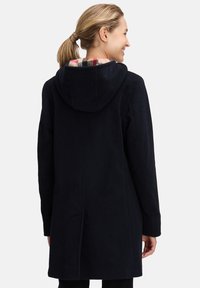 Navy wollen mix jas met een capuchon en een geruite voering. Kenmerkt zich door een recht model, zijzakken en gedetailleerde stiksels op de rug.