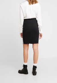 Svart figurnära kjol med scallopad fåll och sidovinjetter, tillsammans med en vit skjorta med knappar och svarta ankelstövlar.