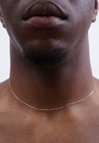 Goldener Kettenanhänger, der auf nackter Haut liegt, mit einem zarten Gliederdesign und glatter Textur. Nahaufnahme des Halses des Trägers.