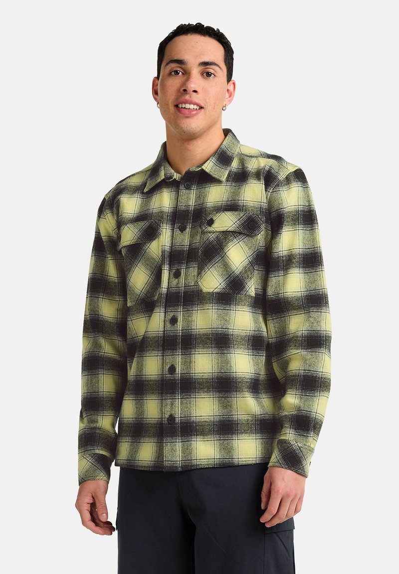 Chemise en flanelle à carreaux jaunes et noirs, avec un devant boutonné, deux poches poitrine et une coupe décontractée. Tissu épais avec un motif texturé.