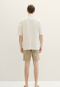 Cămașă scurtă, de culoare bej deschis, cu o croială lejeră, asociată cu pantaloni șort de culoare bej deschis, împăturită la margine, evidențiind un design simplu și o textură moale.