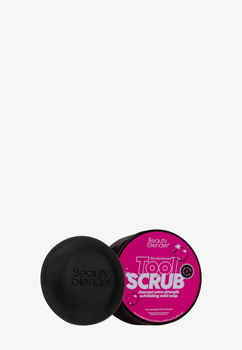Contenitore circolare nero con una texture opaca e il logo "Beauty blender" in rilievo, accanto a un barattolo etichettato di sapone esfoliante rosa.