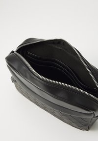 Sort lædertaske med vævet tekstur, lynlåslukning og flere indvendige rum. Glat overflade med mat finish.