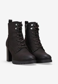 Botas de tobillo de cuero marrón con tacón bloque, que presentan un cierre de cordones en la parte delantera, cremallera lateral y costuras en contraste a lo largo de los bordes.