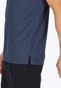 Marineblå atletisk T-shirt med en glat tekstur, korte ærmer og sideslids ved kanten for ekstra komfort og bevægelighed.