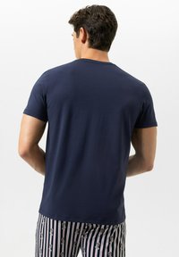 Navyblauw t-shirt met korte mouwen en een ronde hals, met een gladde textuur en een effen ontwerp, gedragen met een broek met patroontjes voorzien van strepen en bedrukte details.