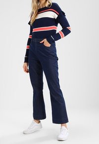 Marinblå randig långärmad tröja med röda och vita ränder, volangdetaljer. Höga mörka denimflares, vita sneakers.