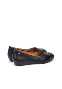 Ballerines en cuir noir avec un petit talon compensé, présentant des coutures diagonales et un petit accent métallique à l'arrière.