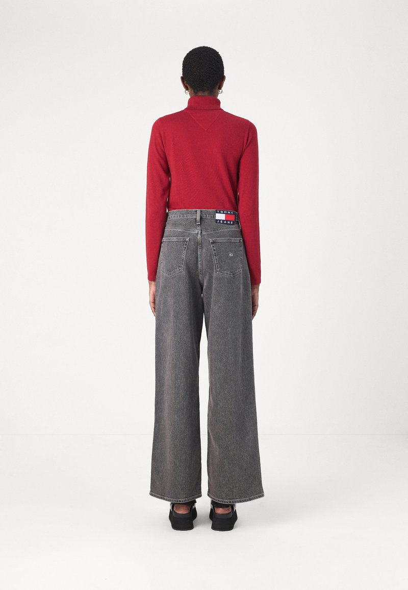 Rote Langarmbluse kombiniert mit hochsitztenden, weit geschnittenen grauen Denim-Jeans, die ein Markenetikett auf der Rückseite tragen. Schwarze Schuhe runden den Look ab.