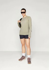 Ελαιόχρωμο μπλουζάκι με μακριά μανίκια, μαύρες βερμούδες, καφέ αθλητικά παπούτσια, λευκές κάλτσες. Το μοντέλο φοράει σκούρα γυαλιά ηλίου και κρατάει μια μαύρη τσάντα πλάτης.