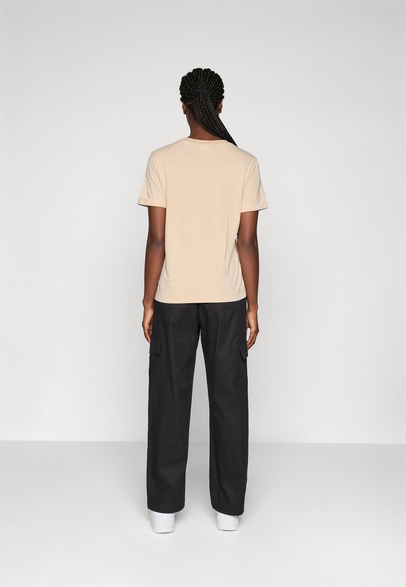 T-shirt in cotone beige con maniche corte, modello slim fit. Indossato con pantaloni cargo neri dotati di tasche laterali e taglio rilassato. Design semplice.