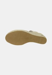 Vista inferiore di una sandaletta con zeppa, caratterizzata da una suola in gomma marrone testurizzata con una leggera curvatura e una parte superiore intrecciata beige con hardware regolabile.