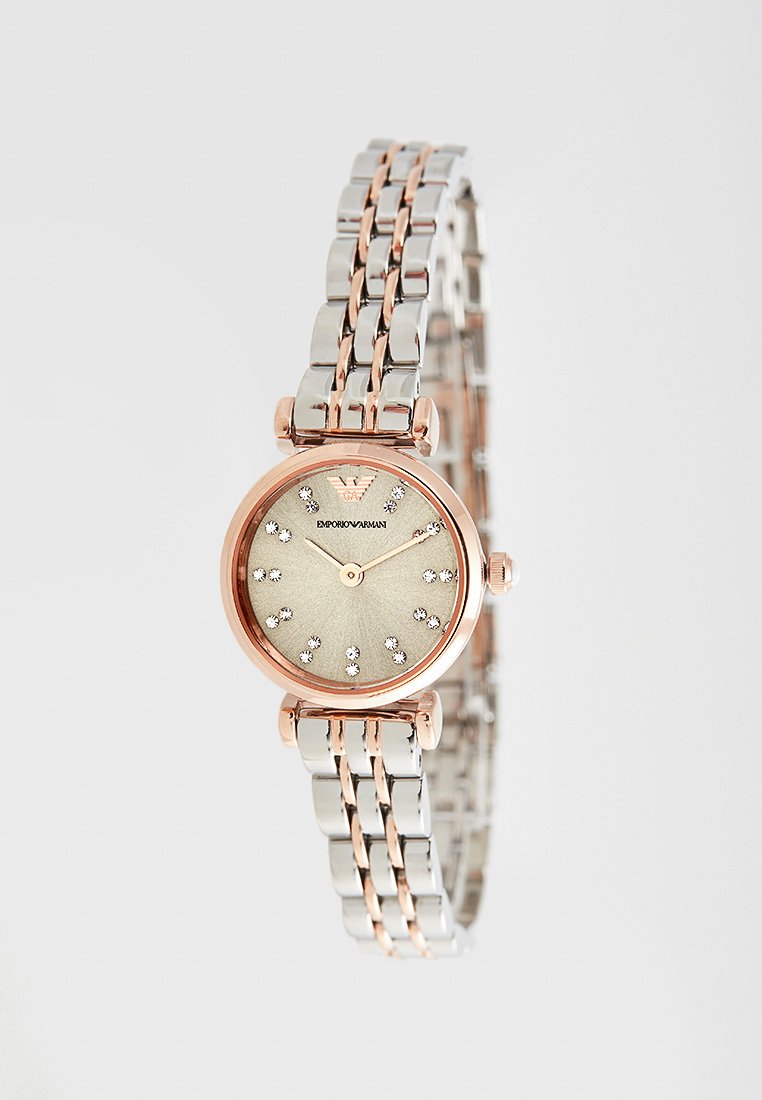 Rundes Uhrengehäuse mit einem goldenen Zifferblatt und Strass-Markierungen, silbernes und roségoldenes Metallarmband sowie einer polierten Oberfläche. Elegante Verschlussdetails.