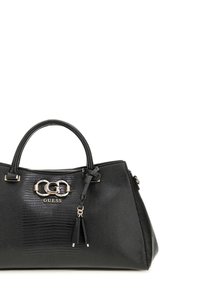 Sac à main noir texturé avec fermeture éclair, poignées doubles, quincaillerie logo argent, et un accent décoratif de pompon. Présente une forme structurée.