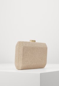 Obdélníkové béžové psaníčko z texturované látky s jemným leskem. Má zlaté zapínání a hladké okraje. Minimalistický design.