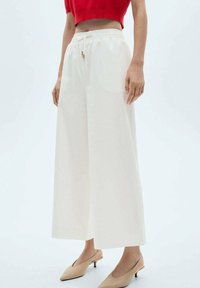 Witte wijde broek met een trekkoord in de taille, een soepele textuur en twee zijzakken. De stof is lichtgewicht en soepel.