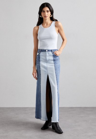 Denim maxi skirt featuring a front slit, varying shades of blue, and pockets. Paired with a gray tank top and black ankle boots.