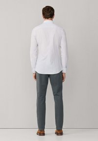 Witte gestreepte overhemdd met button-down kraag, gecombineerd met een grijze broek en bruine schoenen, gezien vanuit de achterkant.