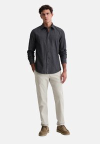 Dunkelgraues Hemd mit Knopfverschluss aus einem strukturierten Stoff, kombiniert mit hellbeigen Hosen und braunen Schuhen. Figurbetonter Schnitt mit klassischem Kragen.