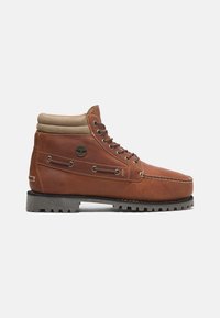 Botte en cuir marron avec col rembourré beige, bout rond, six œillets et semelle extérieure en caoutchouc avec crampons pour la traction. Logo Timberland sur le côté.