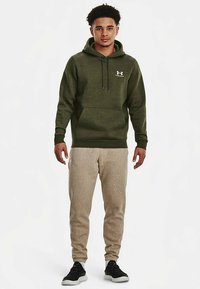 Zöld pamut kapucnis pulóver elülső zsebbel és húzózsinóros kapucnival, világos bézs színű kényelmes jogging nadrággal párosítva. Fekete sportcipővel egészül ki az összkép.