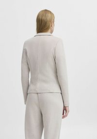 Ljust beige skräddarsydd blazer med en strukturerad form, mjuk textur och detaljerade sömmar bak, kombinerad med matchande byxor.