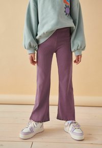 Pantalons évasés violets à côtes avec un ourlet festonné, associés à des baskets blanches ornées d'accents lavande et de rubans ; sweat-shirt menthe au-dessus.