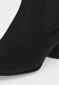 Bottine noire à bout pointu, talon bloc et panneau latéral élastique pour un enfilage facile.