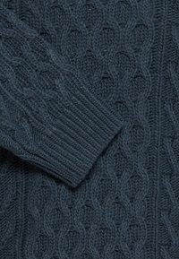 Tissu tricoté bleu foncé avec un motif torsadé et un poignet côtelé plié sur la surface texturée.