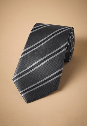 Schwarze Krawatte mit diagonalen silbernen und dunkelgrauen Streifen, auf einer beigen Oberfläche gerollt.