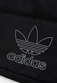 Černá sportovní taška z textilu s velkým bílým logem Adidas trefoil, hladká textura a vodorovné pruhy v designu loga.