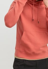 Sudadera con capucha de manga corta en color coral, confeccionada con tela suave, con bolsillo delantero tipo canguro, cordones ajustables y puños y dobladillo acanalados.