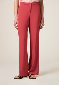 Spodnie szerokie w kolorze koralowym, wykonane z gładkiego materiału. Posiadają zapięcie na guzik z przodu oraz subtelne kieszenie w szwach bocznych.