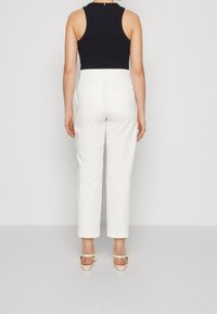 Pantaloni bianchi a vita alta e top smanicato nero a coste, che mettono in evidenza un design aderente con una texture liscia. La vista posteriore evidenzia la vita e le tasche.
