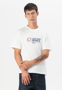 Witte katoenen t-shirt met een grafisch ontwerp met de tekst "JACK & JONES" in blauw en rood. Korte mouwen en een ronde hals.