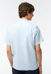 Camicia azzurra a maniche corte realizzata in un tessuto leggero e liscio, con colletto standard e orlo diritto. Senza fantasie né dettagli.