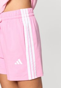 Rosa treningsshorts med hvite striper på siden og en hvit logo nederst til venstre. Elastisk midjebånd for komfort og god passform.