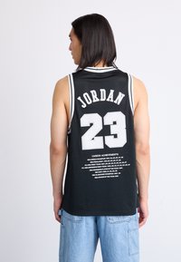 Zwarte basketbalsjersey met "JORDAN" en het nummer "23" in het wit. Meshmateriaal met witte afwerking en bedrukte carrière-prestaties op de achterkant.