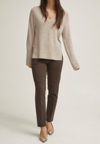 Beige stickad tröja med V-ringning och ribbad kant, parat med åtsittande bruna byxor och spetsiga klackar med ormskinnsmönster. Texturerade tyg detaljer synliga.