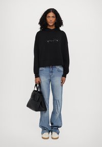 Black cropped hoodie with embossed logo, paired with light blue wide-leg jeans featuring a subtle pattern, and a black handbag. White sneakers.