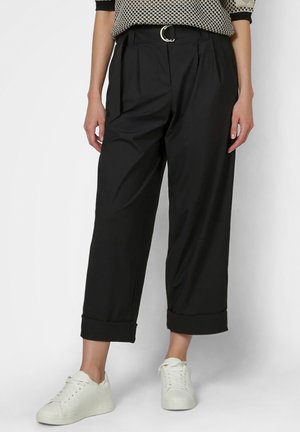 Woman wearing black high-waist wide-leg cropped pants with cuffed hems, a belt with a round buckle, and white sneakers.