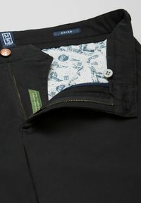 Zwarte chino broek met een rits, voorzien van een gestreepte binnenvoering en een groen label aan de binnenkant van de tailleband. Zichtbare metalen accenten.